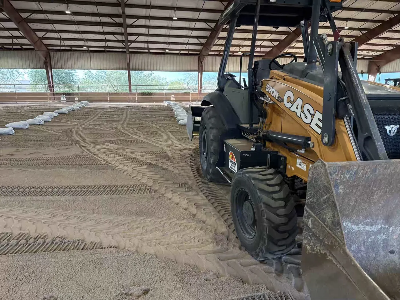 Loader finishing a graded arena surface with sandbag edge control